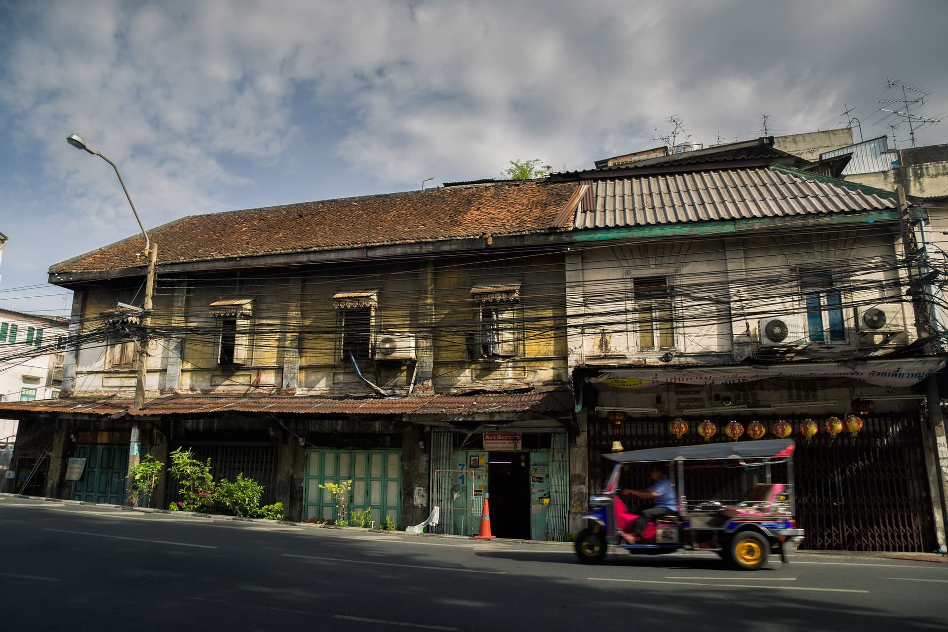 Một chiếc tuk-tuk lướt qua dãy nhà phố cũ trong khu phố cổ Bangkok giữa ban ngày.