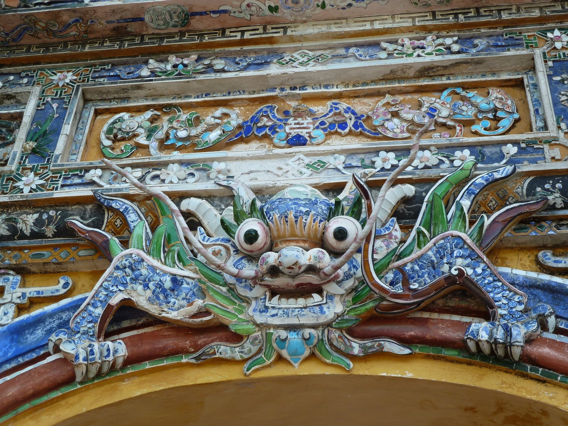 A dragon built up from cut porcelain shards, glazed blue and white, set above an archway.