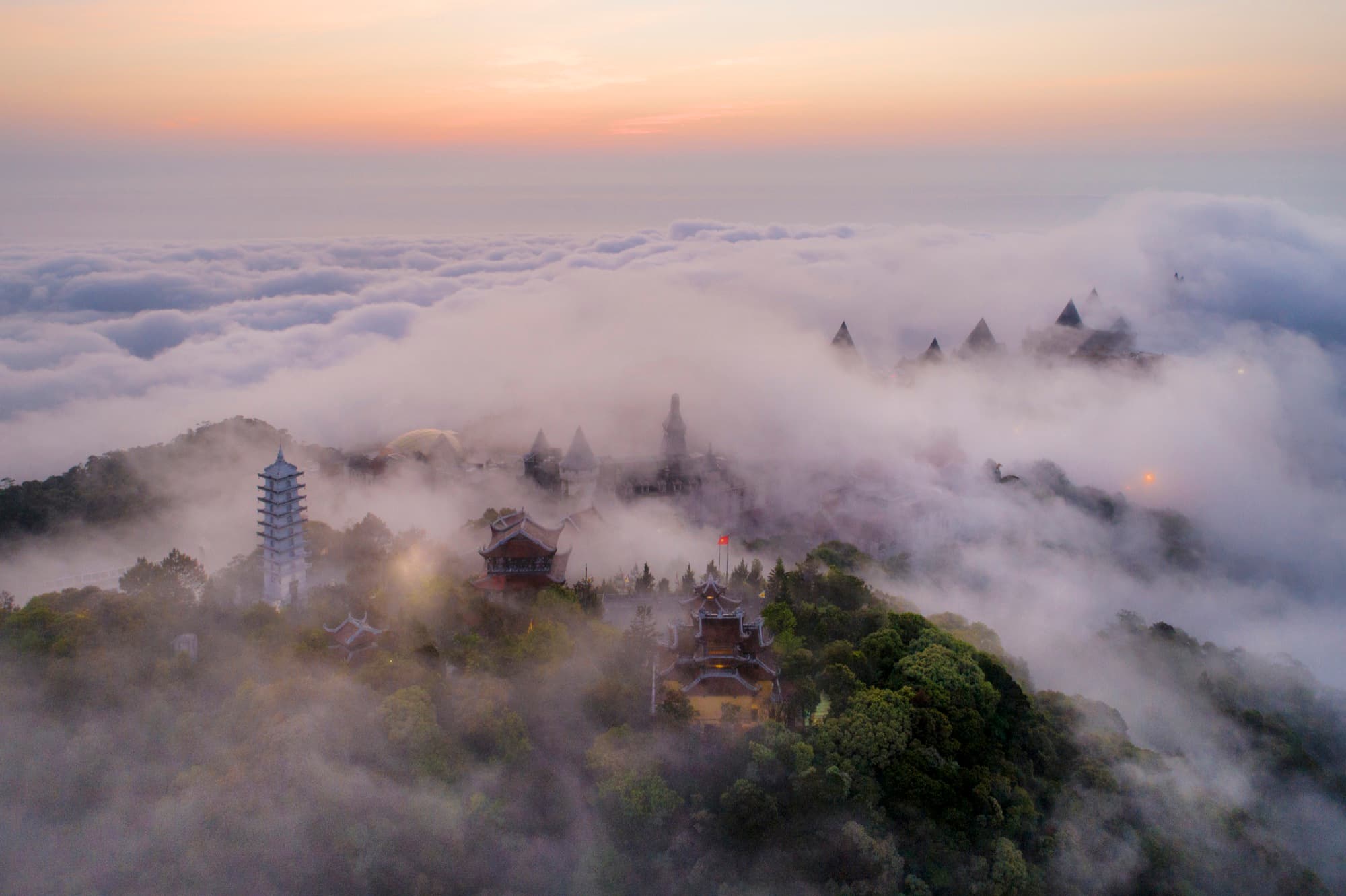 Ancient Thai temples emerging from mountain mist at sunrise — aerial photography