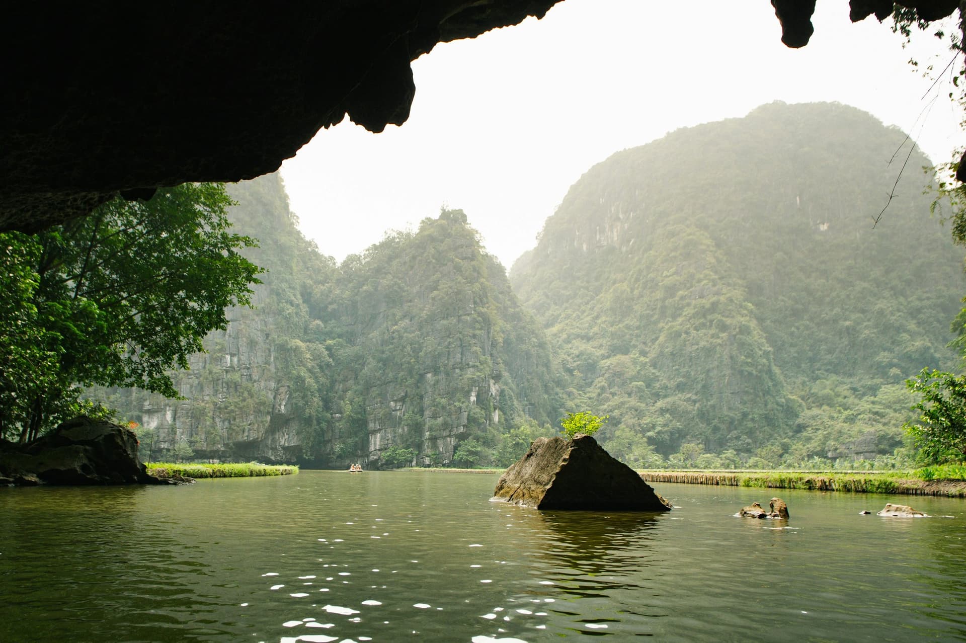 A karst river gorge seen from the mouth of a cave, still green water running out towards the far peaks.