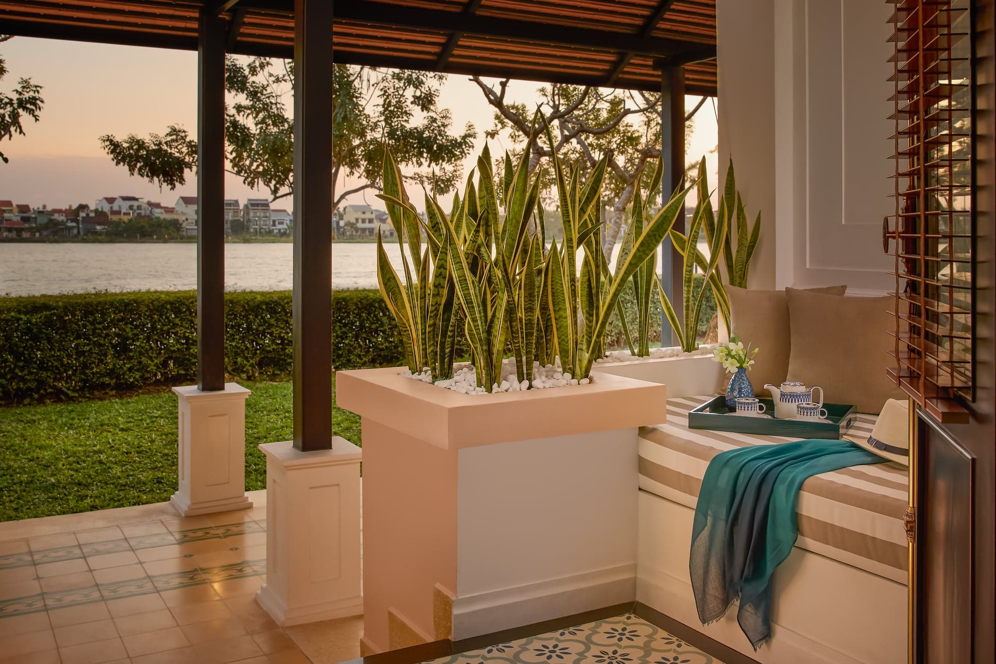 พอร์ชของ Thu Bon River Suite ที่ Anantara Hoi An Resort มีเตียงเดย์เบด กระถางต้นไม้ โดยมีแม่น้ำอยู่เบื้องหลัง