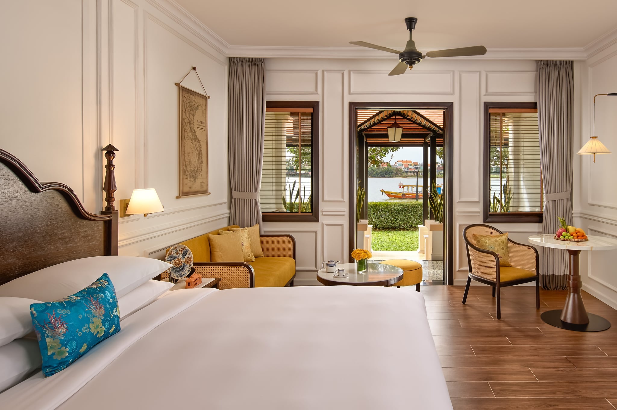 A Thu Bon River Suite with a carved wooden bed, a lounge corner and open doors onto a porch facing the river