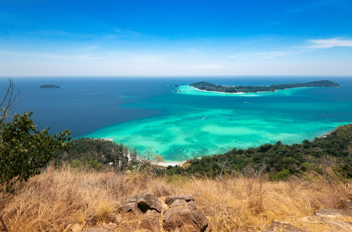 Turquoise reef water and offshore islands seen from a headland in southern Thailand, the coastal half of the classic range a European agent can build a first trip around.