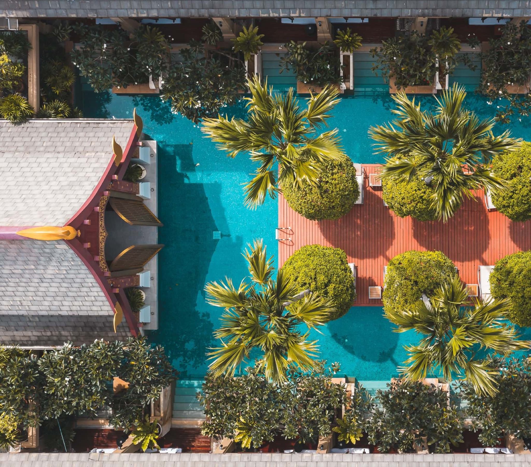 Vista aérea de la piscina turquesa, las palmeras y el tejado de estilo pabellón tailandés de Burasari Phuket, hotel asociado de Pai Dai DMC en Phuket, Tailandia