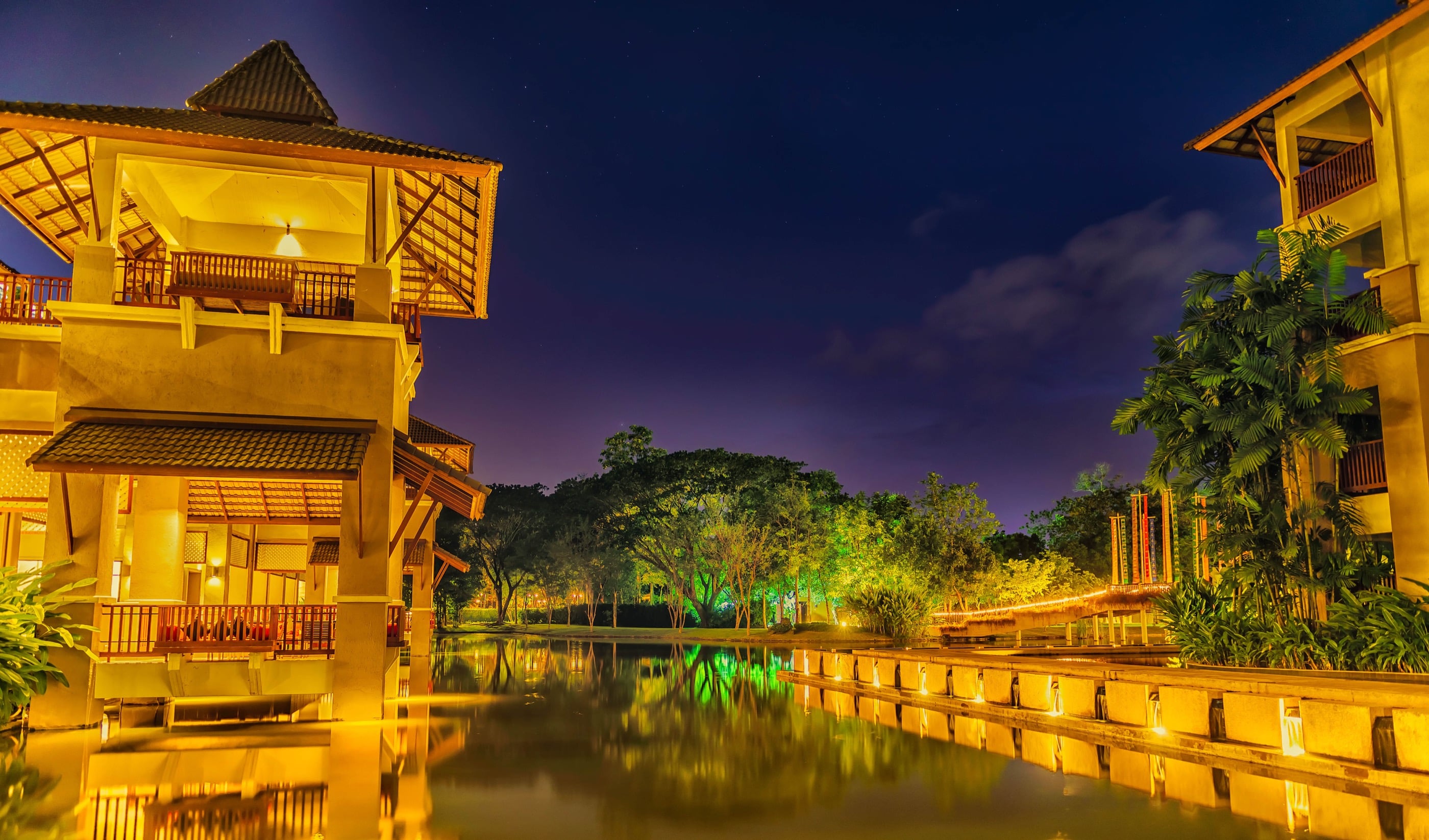 Lanna-roofed pavilions with warmly lit balconies mirrored in a still lagoon at blue hour, the register of a northern highland retreat.