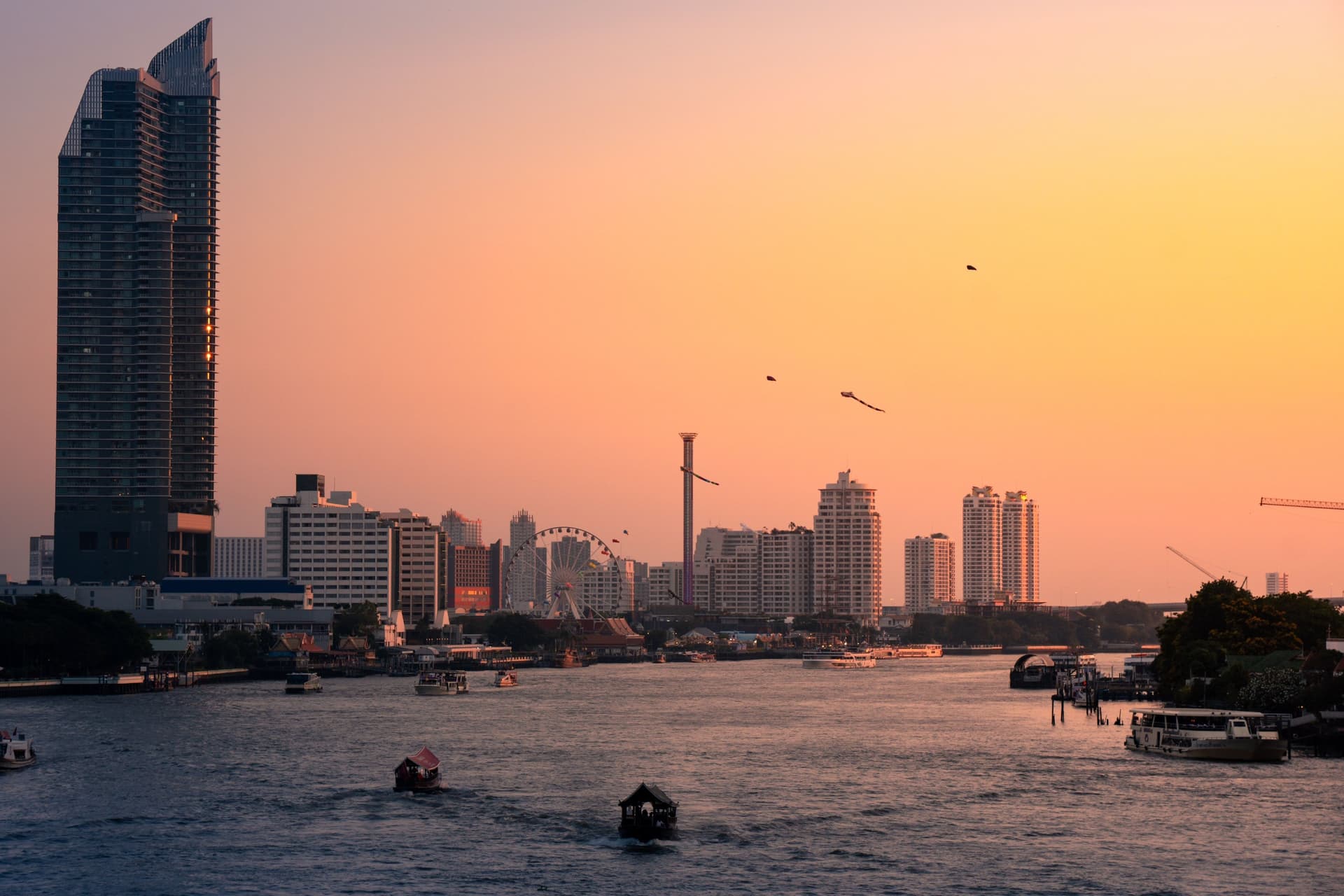 Đường chân trời Bangkok lúc hoàng hôn bên sông Chao Phraya, vài con thuyền nhỏ trên mặt nước.