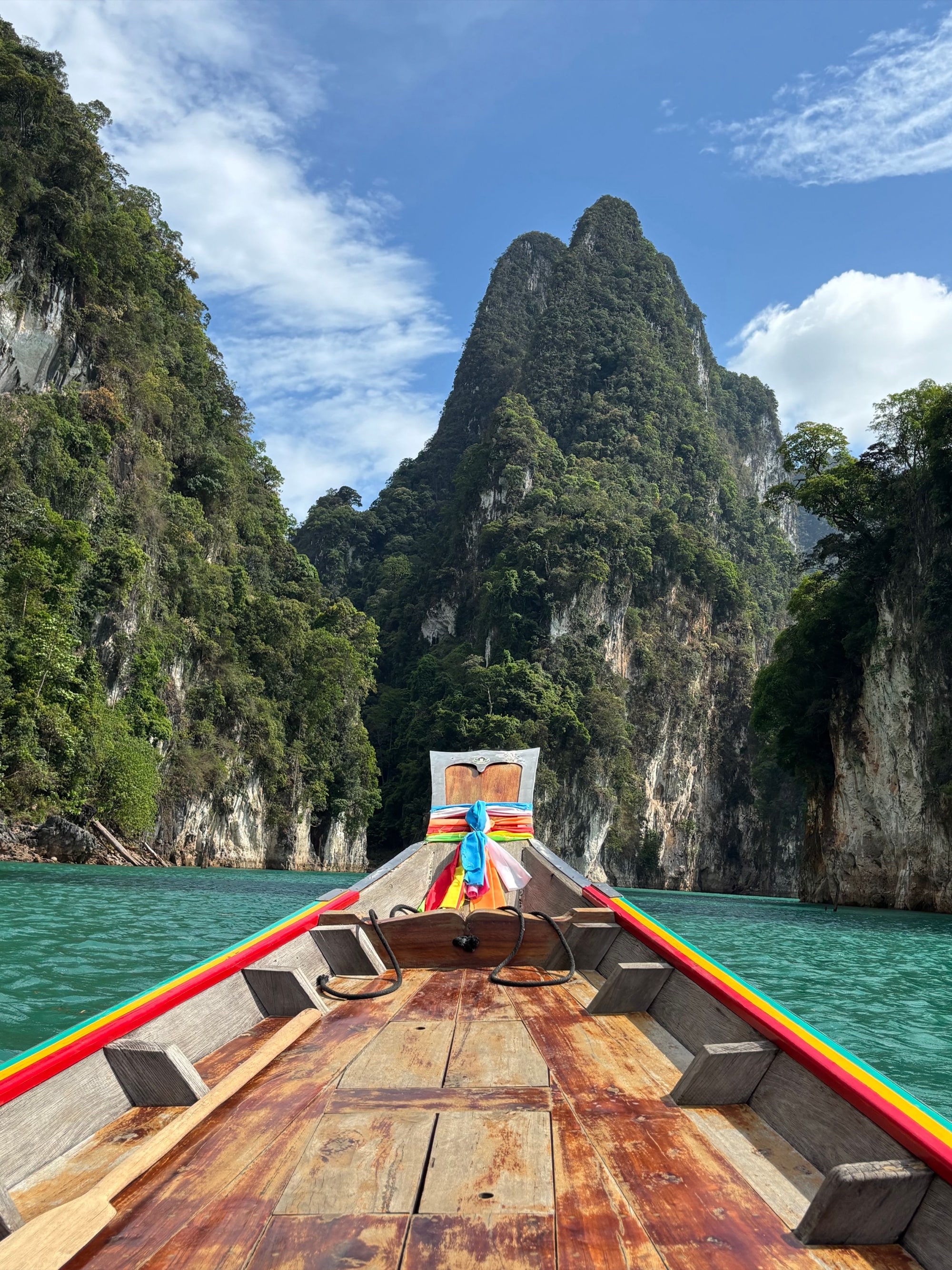 Vista desde la proa de una tradicional barca tailandesa de cola larga que cruza una laguna esmeralda hacia imponentes picos kársticos de piedra caliza cubiertos de selva, Phang Nga, Tailandia