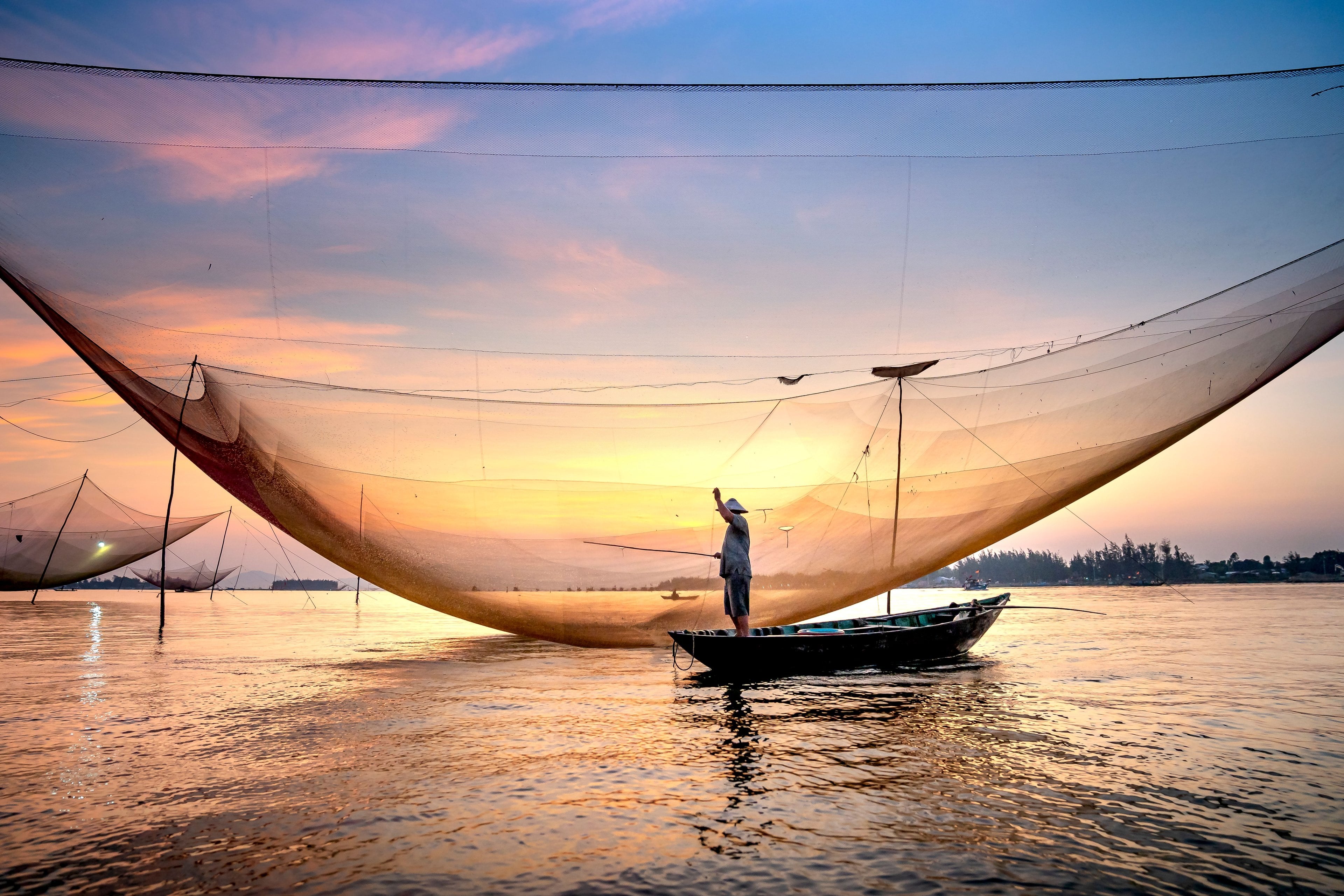 صياد يقف في قاربه تحت شبكة رفع كبيرة عند الغروب قرب هوي آن (Hoi An)