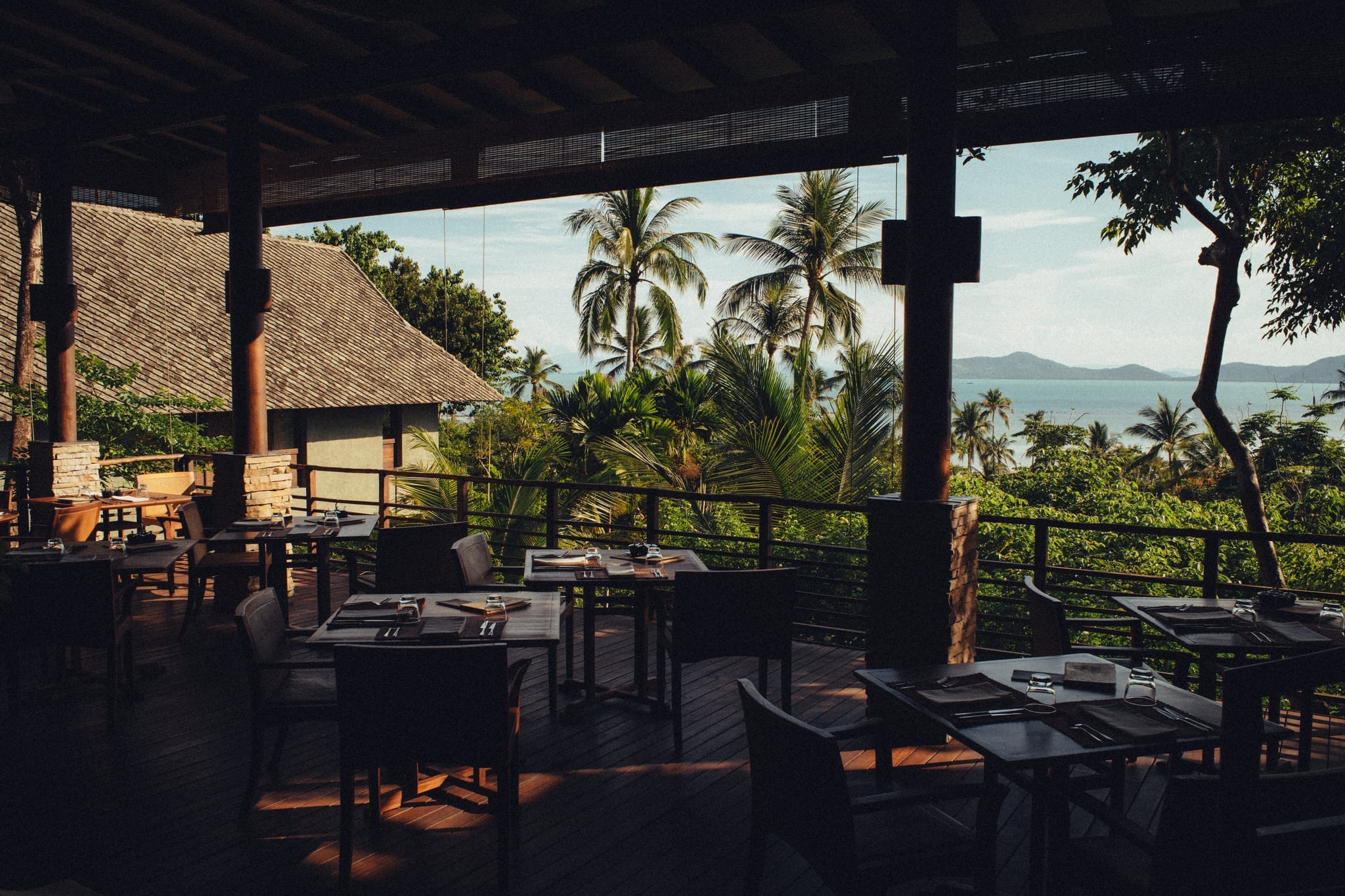 Tables laid on the open-sided deck of Soma Restaurant, with palms and the sea beyond