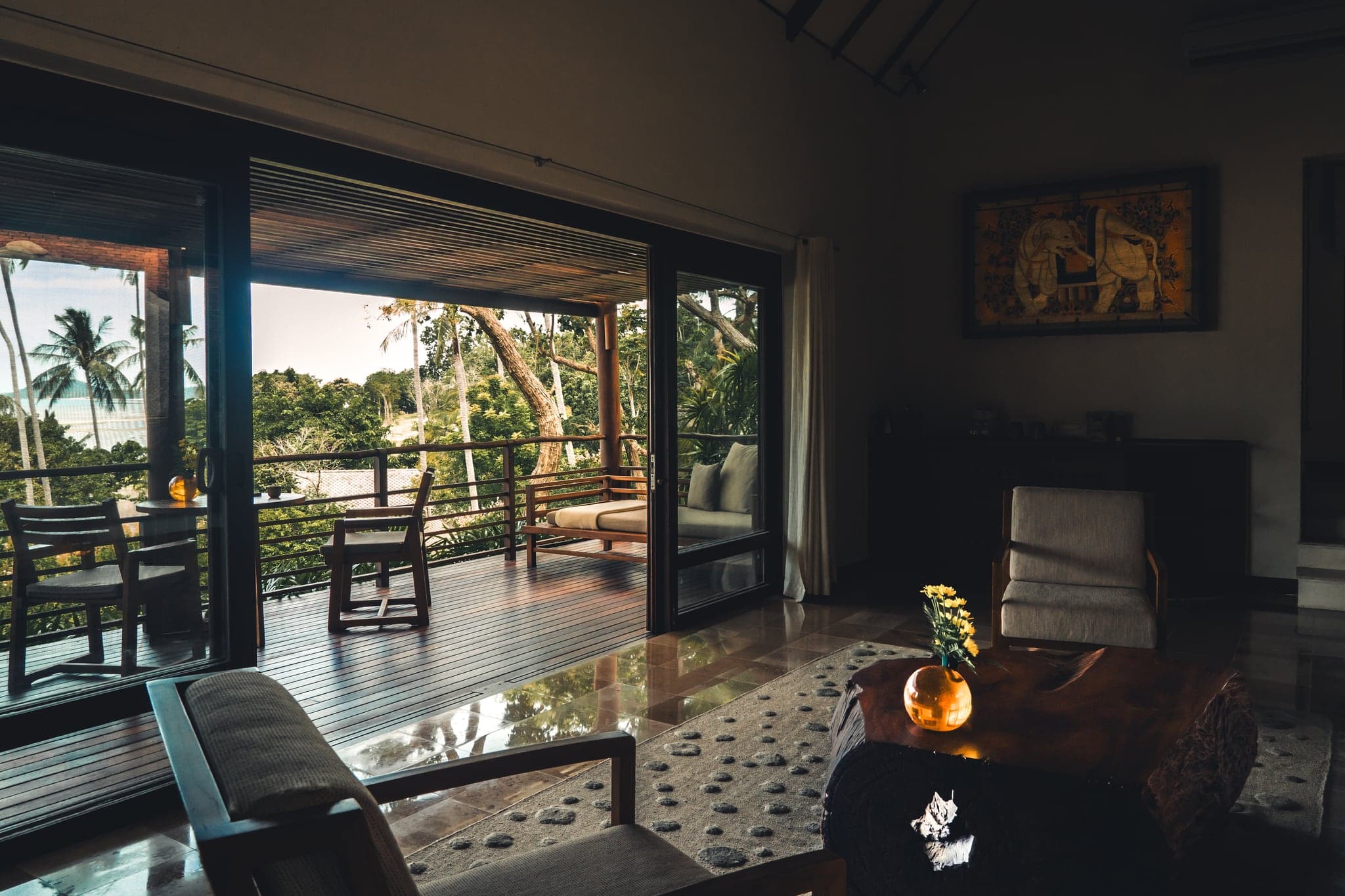 El salón de una villa de Kamalaya, con muebles de madera y puertas abiertas a una terraza, con palmeras y el mar al fondo