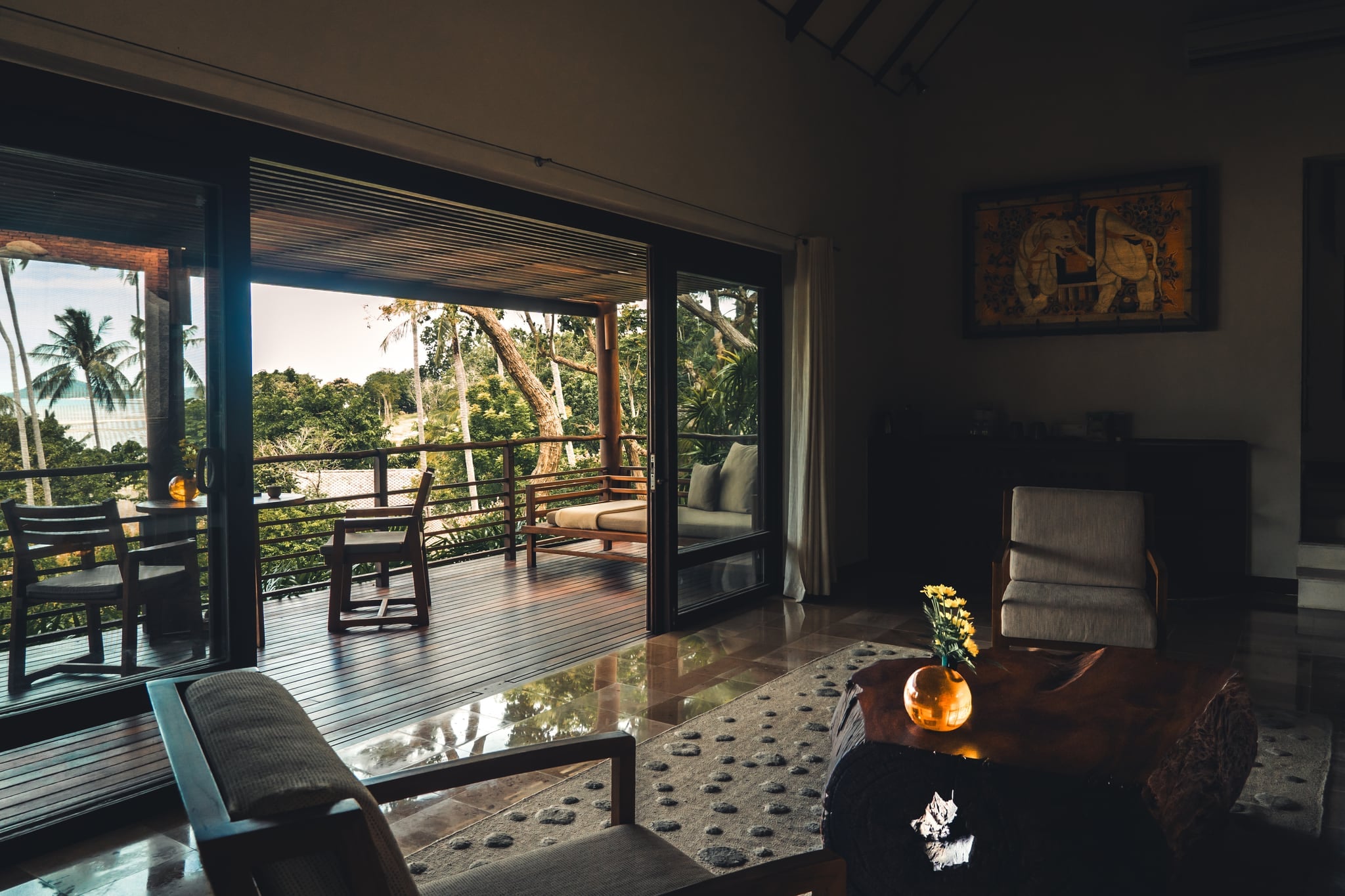 A villa living room at Kamalaya with wooden furniture and open doors onto a terrace, with palms and the sea beyond
