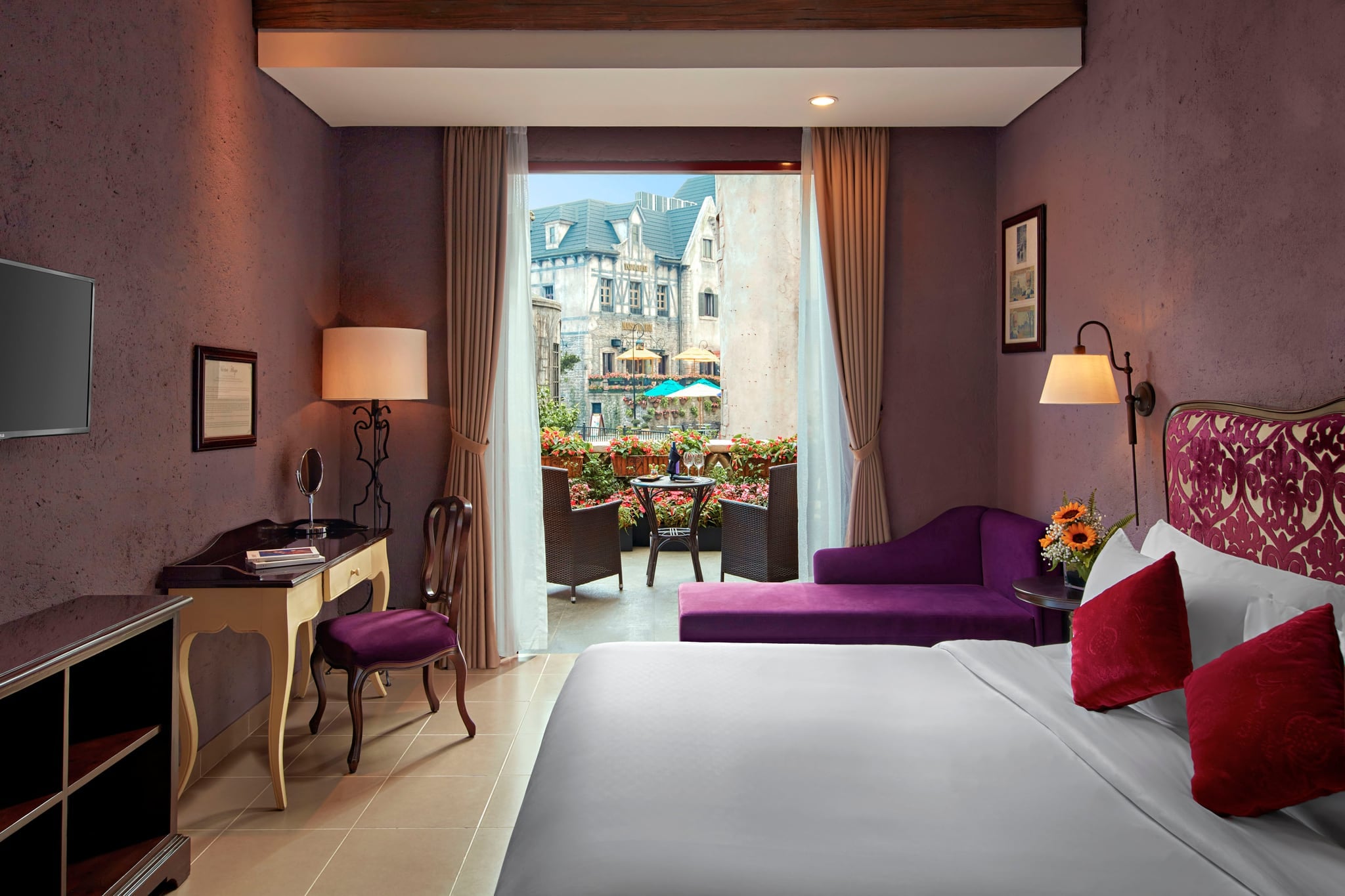 A guest room with the balcony door open onto wicker chairs, flower boxes and the French Village beyond