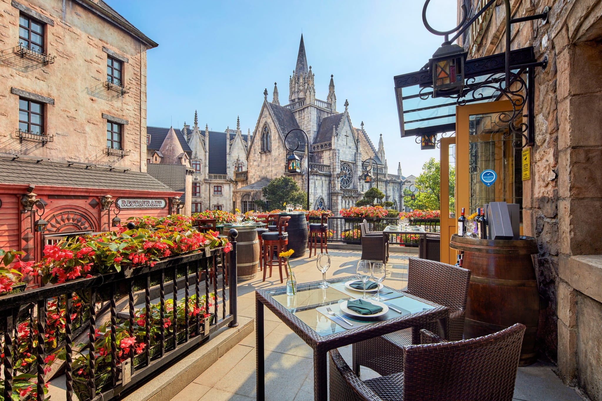 Tables set on the Maison du Roi terrace among red flowers, facing a Gothic-style stone church