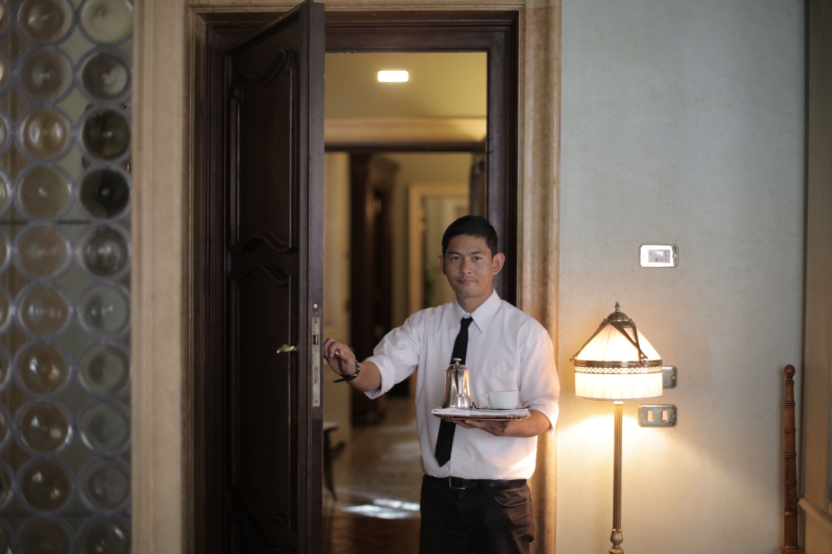 A hotel server presenting a tray at a guest-room door, the quiet service continuity of one team on the ground.