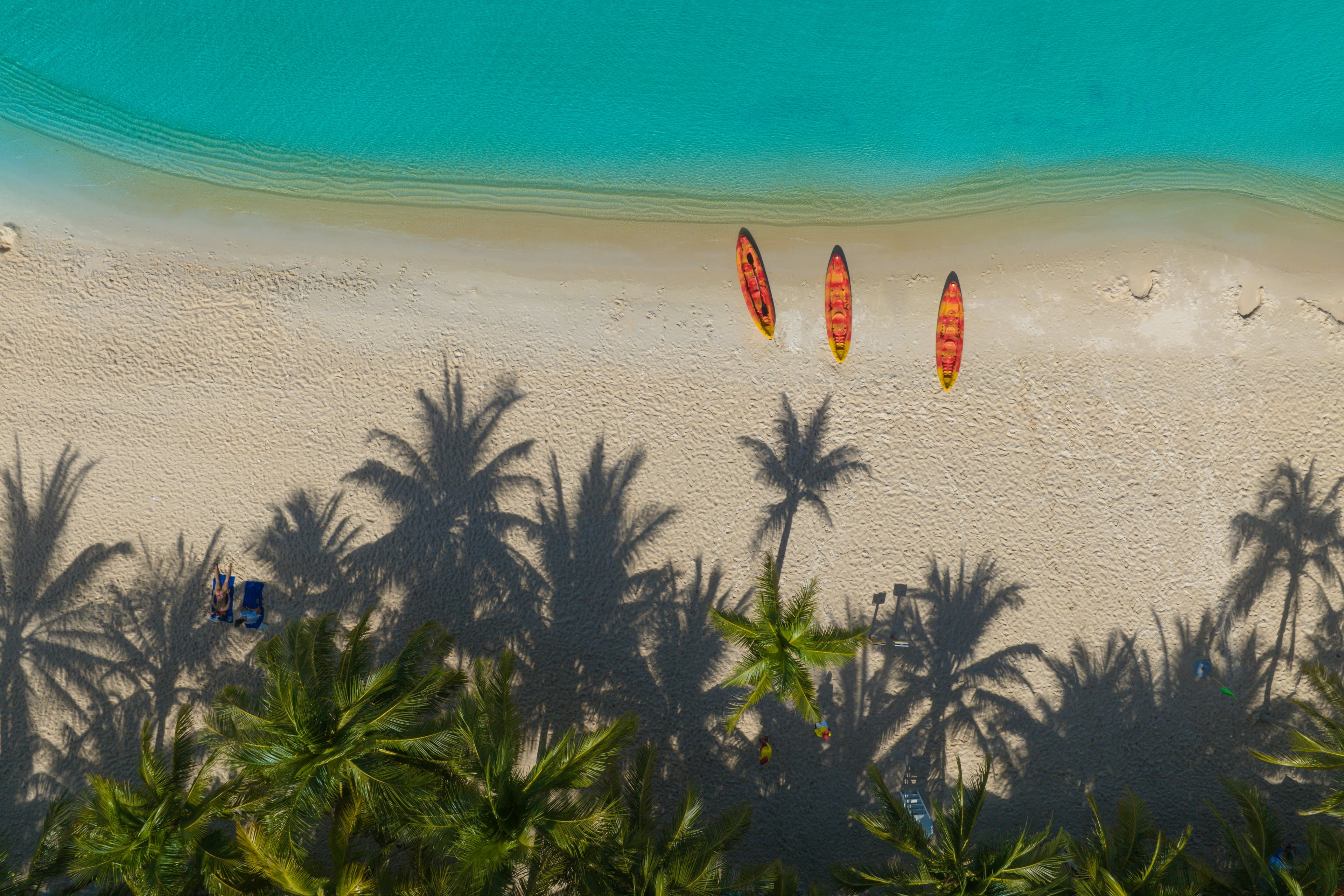 Three kayaks on Khem Beach, with turquoise water and palm shadows across the sand