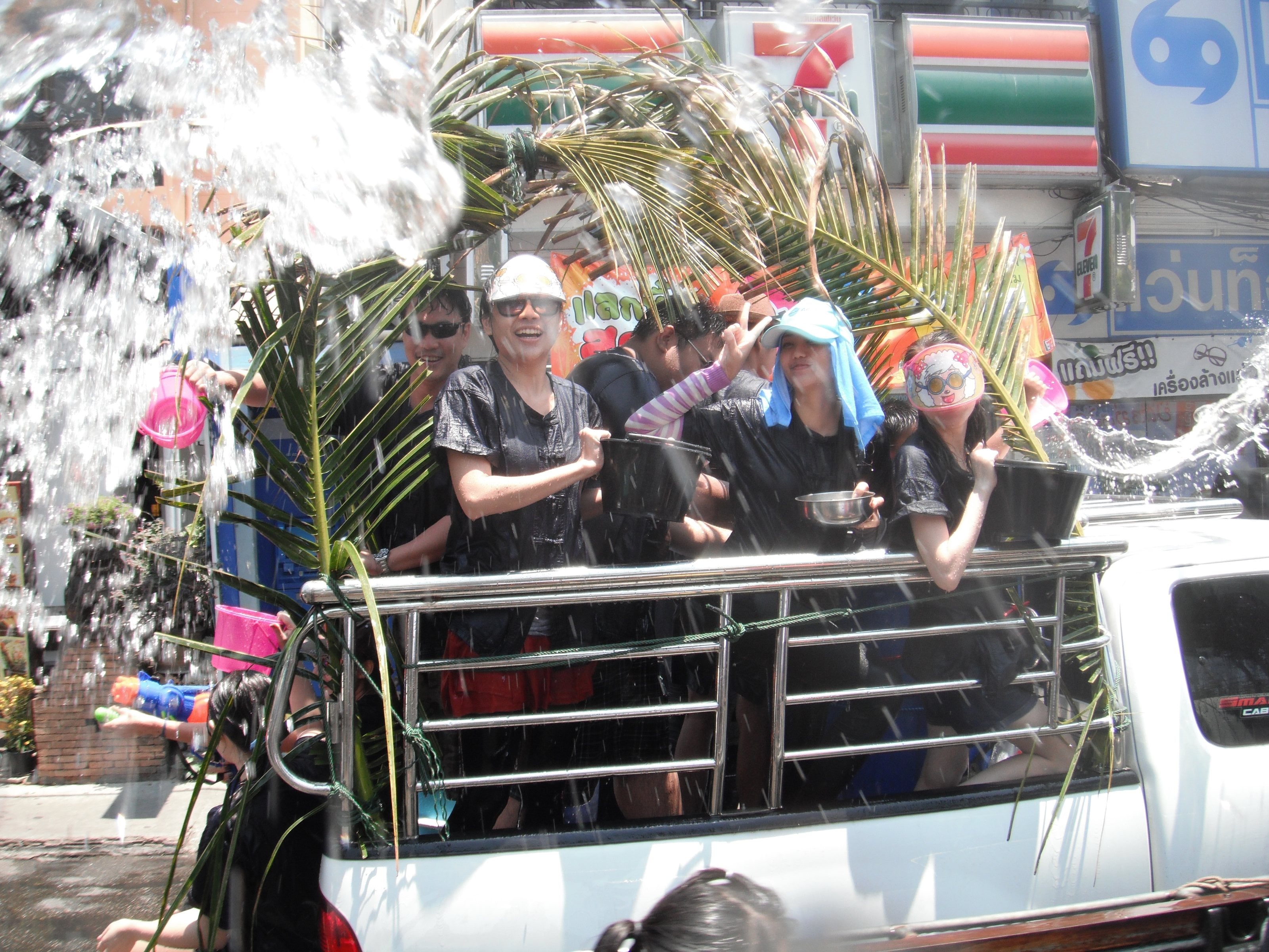 Passengers in the back of a pickup in Chiang Mai sheltering behind palm fronds as water hits them.