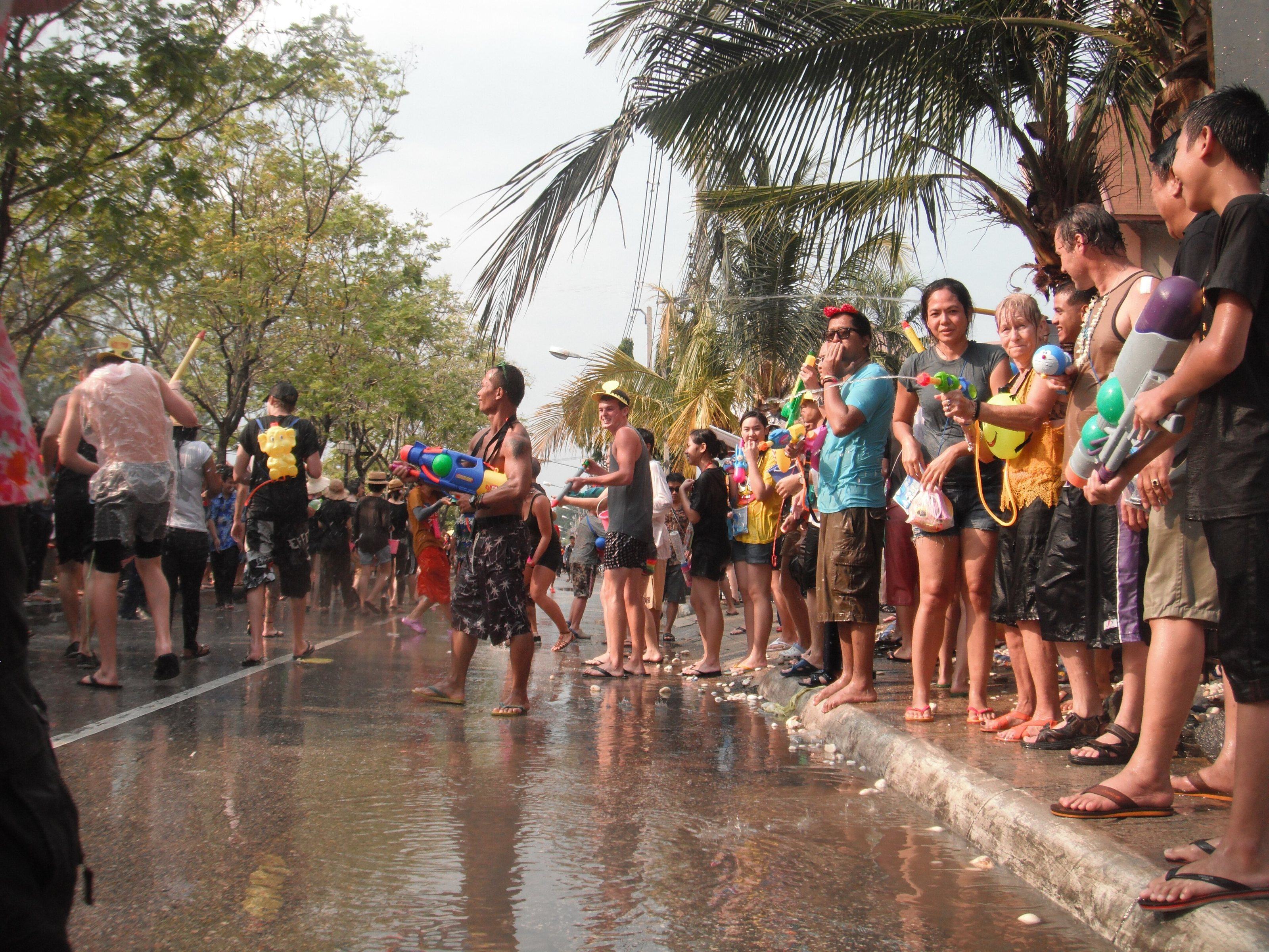A long line of people with water guns along a wet street lined with palms in Chiang Mai.