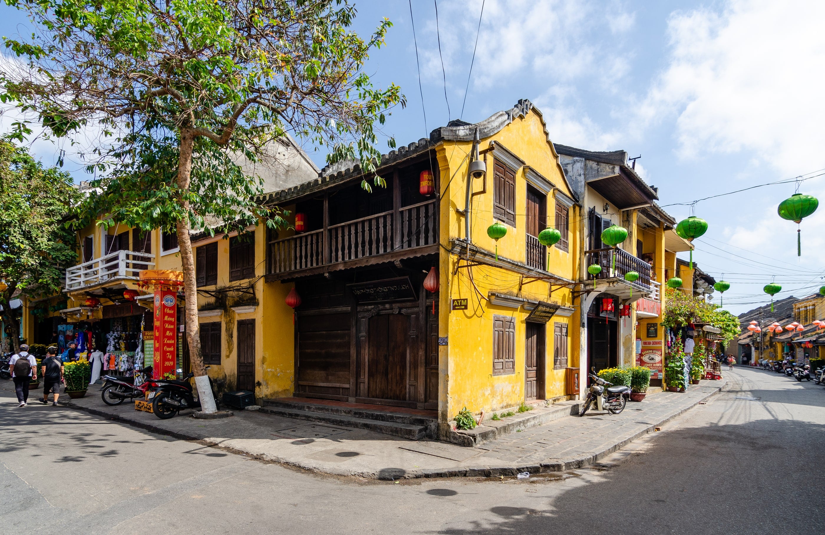 Ochre shophouses with wooden balconies and green lanterns on a corner in Hoi An Ancient Town.