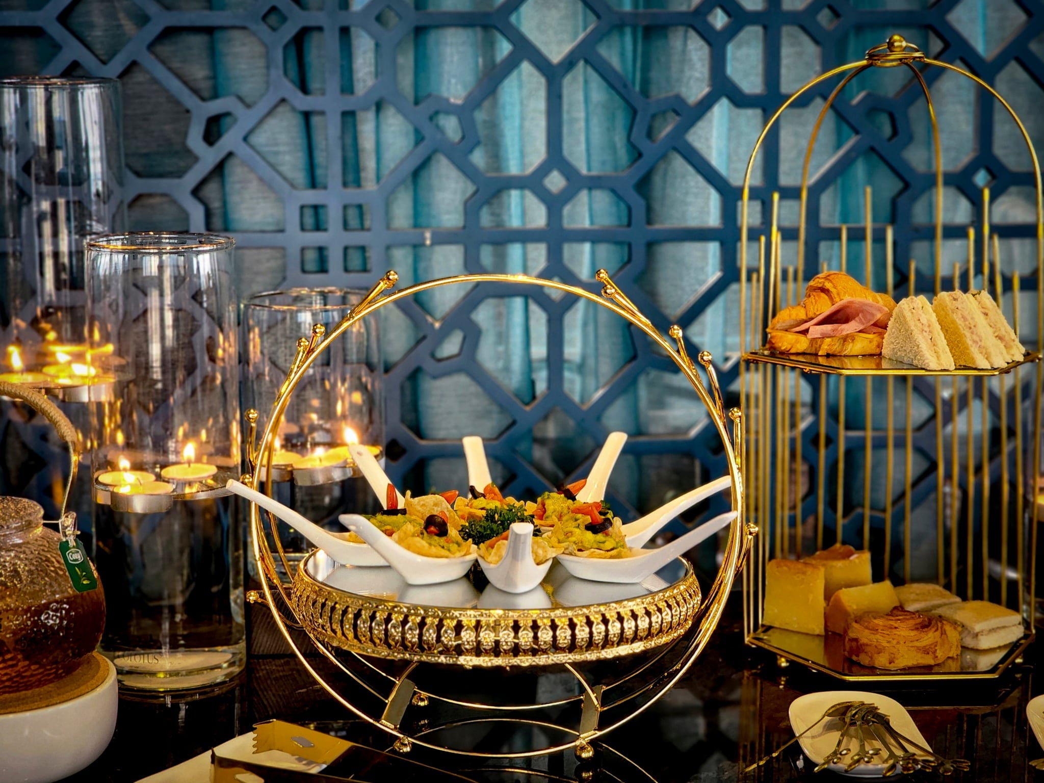 Afternoon tea at The Odys: savoury bites in porcelain spoons on a gold stand, with sandwiches, pastries and candles