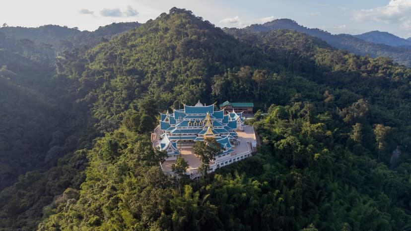 Wat Pa Phu Kon stands alone on its forested mountain, the white vihara and tiered teal roofs rising from unbroken national reserved forest.