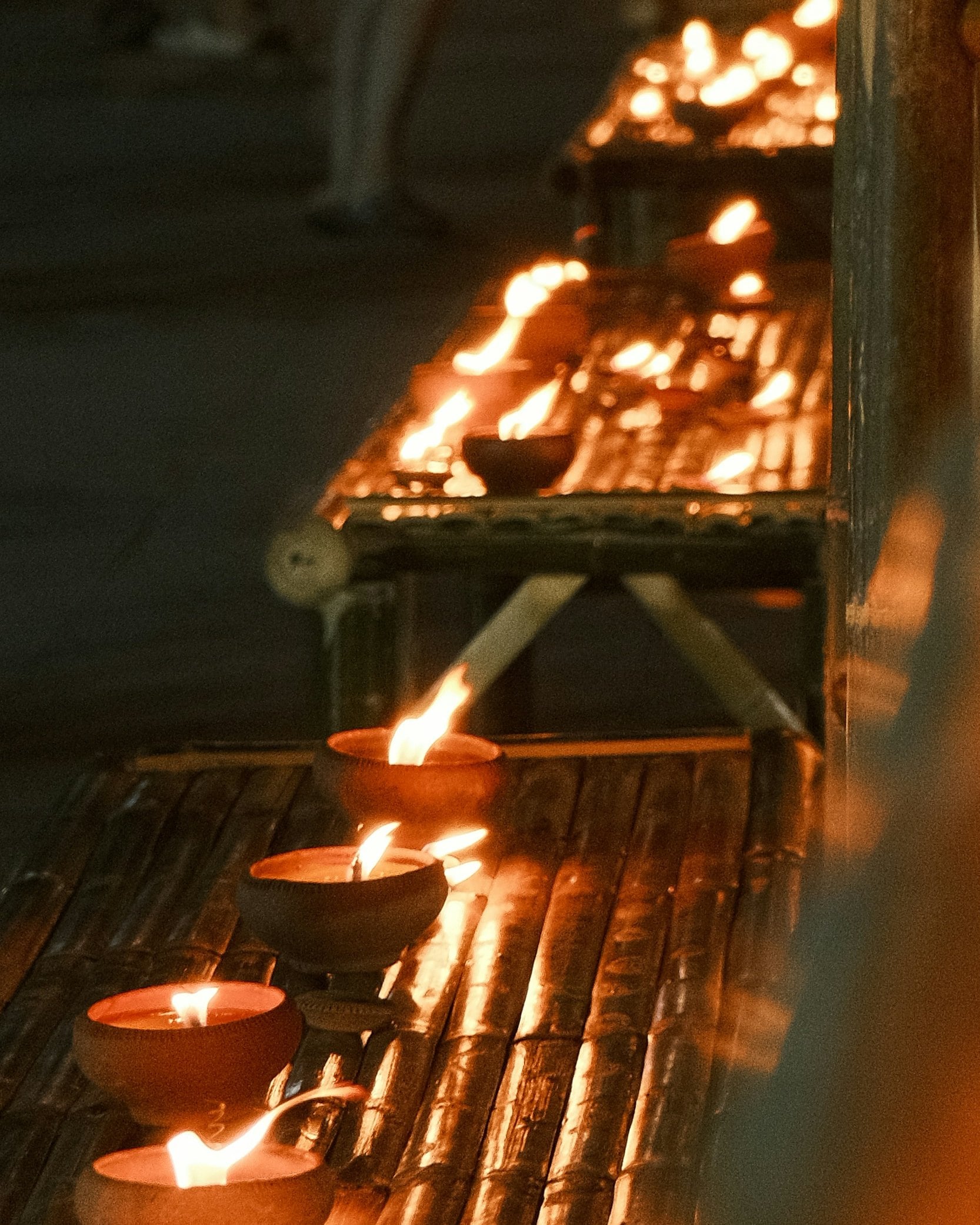 Những hàng đèn nhỏ cháy trong chén đất nung trên giá tre về đêm, những chiếc gần nhất rõ nét, phần còn lại mờ dần.