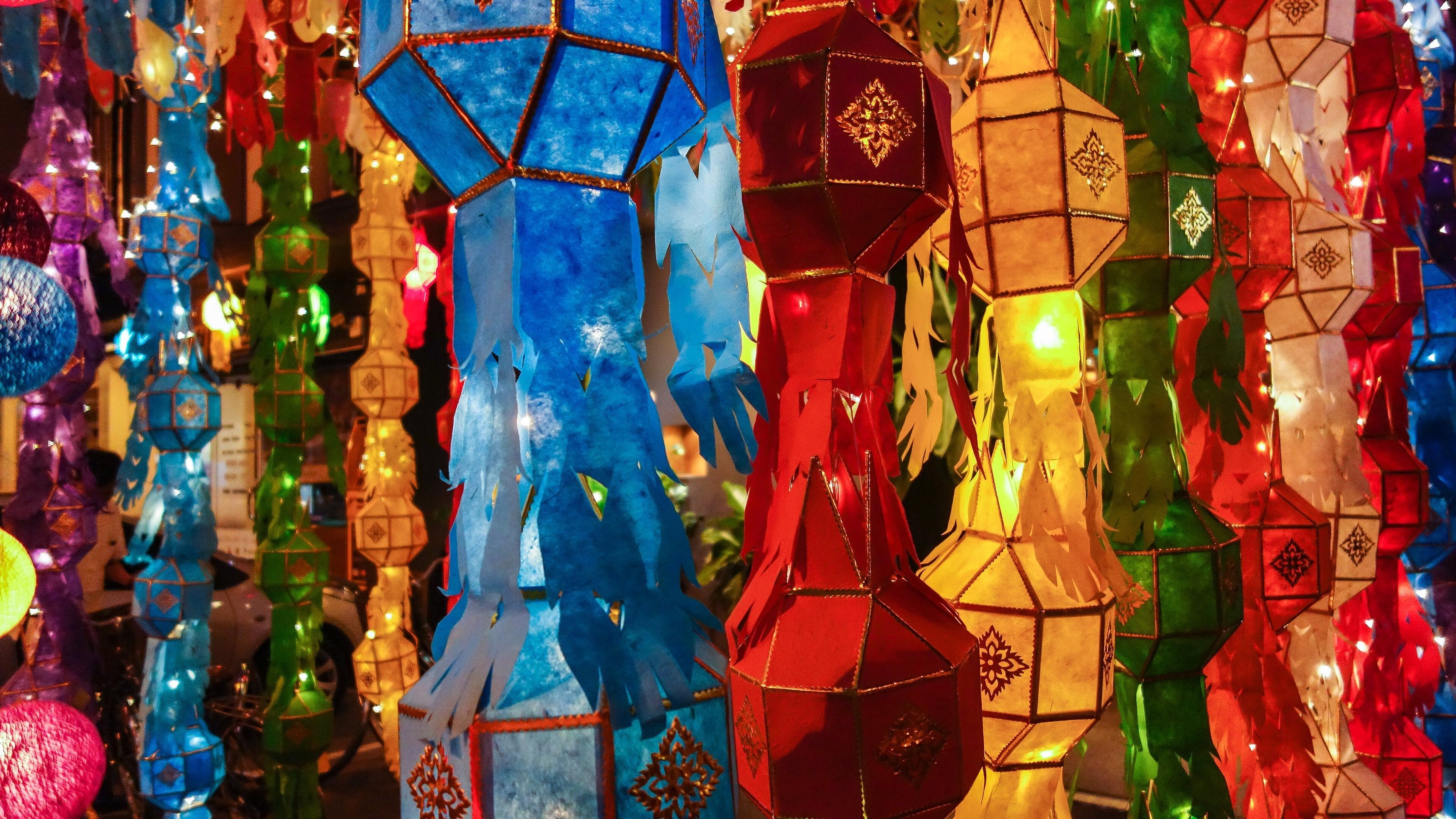 Tall paper lanterns in blue, red, yellow and green, lit from inside and hung close together.