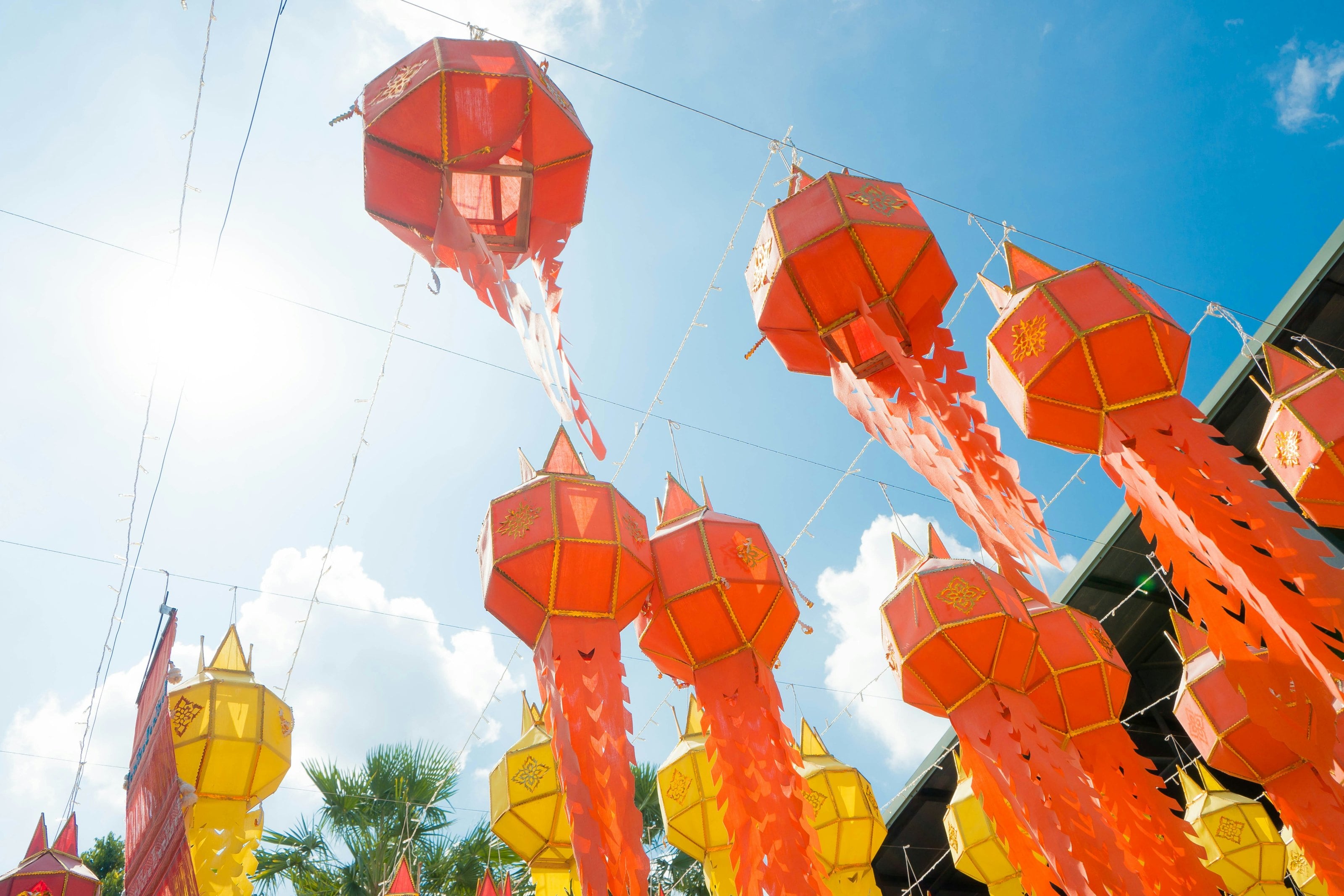 Red and yellow lanterns with long paper tails hanging against a blue sky.