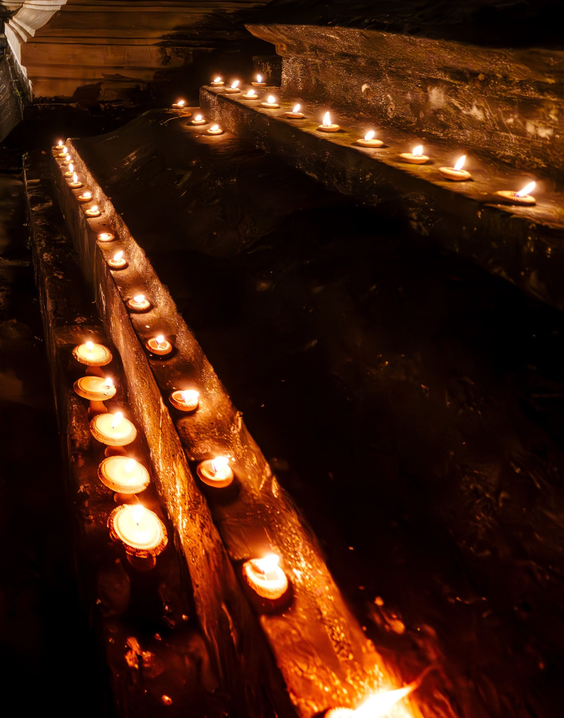 Rows of small clay oil lamps burning along the steps of a temple at night.